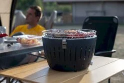 LotusGrill XL Hybrid Houtskoolbarbecue - Rood -Buiten Kamperen lotusgrill in gebruik met toppy shirtje 2